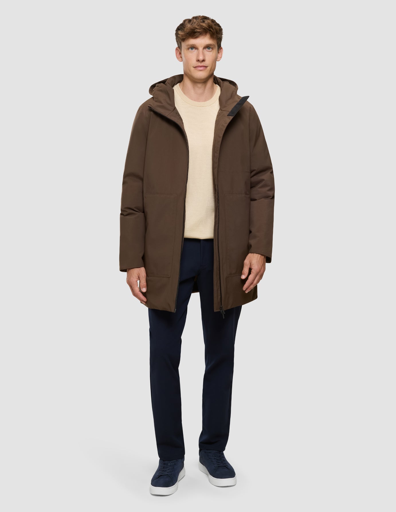 En man bär en Utility Jacket i färgen Saddle Brown över en beige tröja och mörka byxor.
